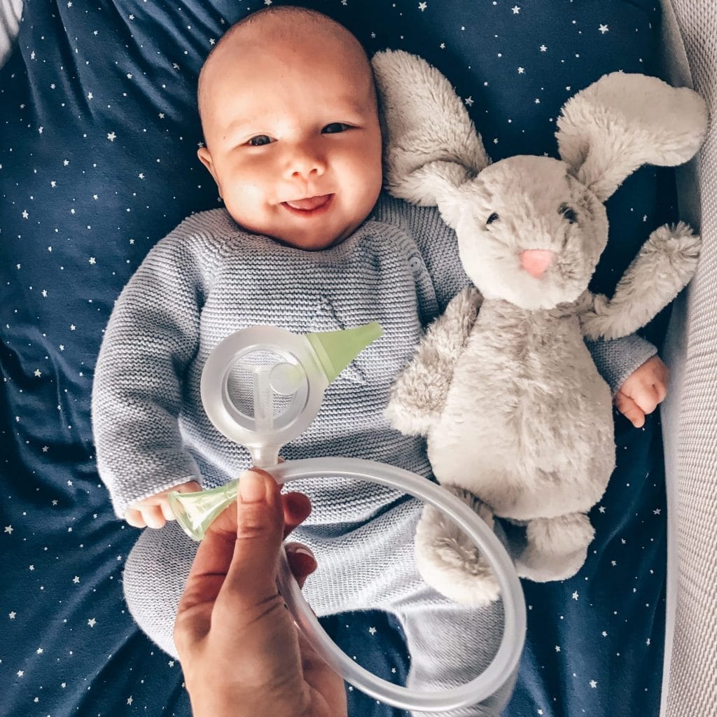 Mosolygó csecsemő fölé valaki Nosiboo Eco kézi orrszívót tart